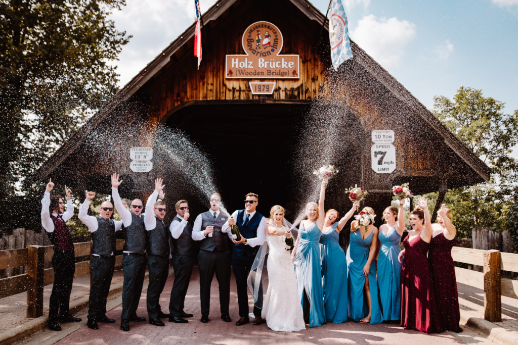 Wedding party sprays champagne in front of covered Bavarian Bridge