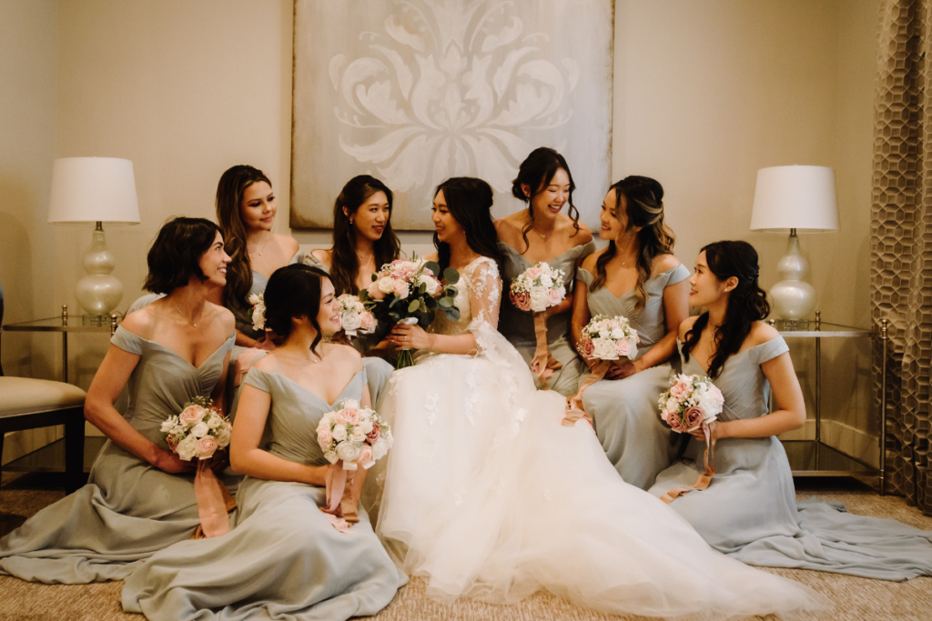 Brides and bridesmaids sitting on a couch laughing in bridal suite