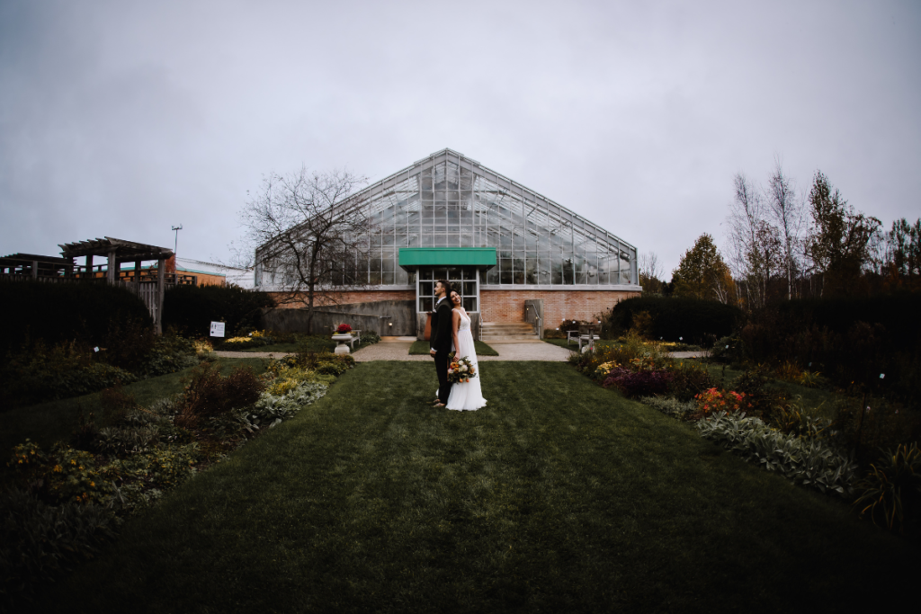 Bride and groom pose in front of greenhouse